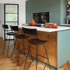 wooden kitchen flooring, green and gold island unit with brown stools
