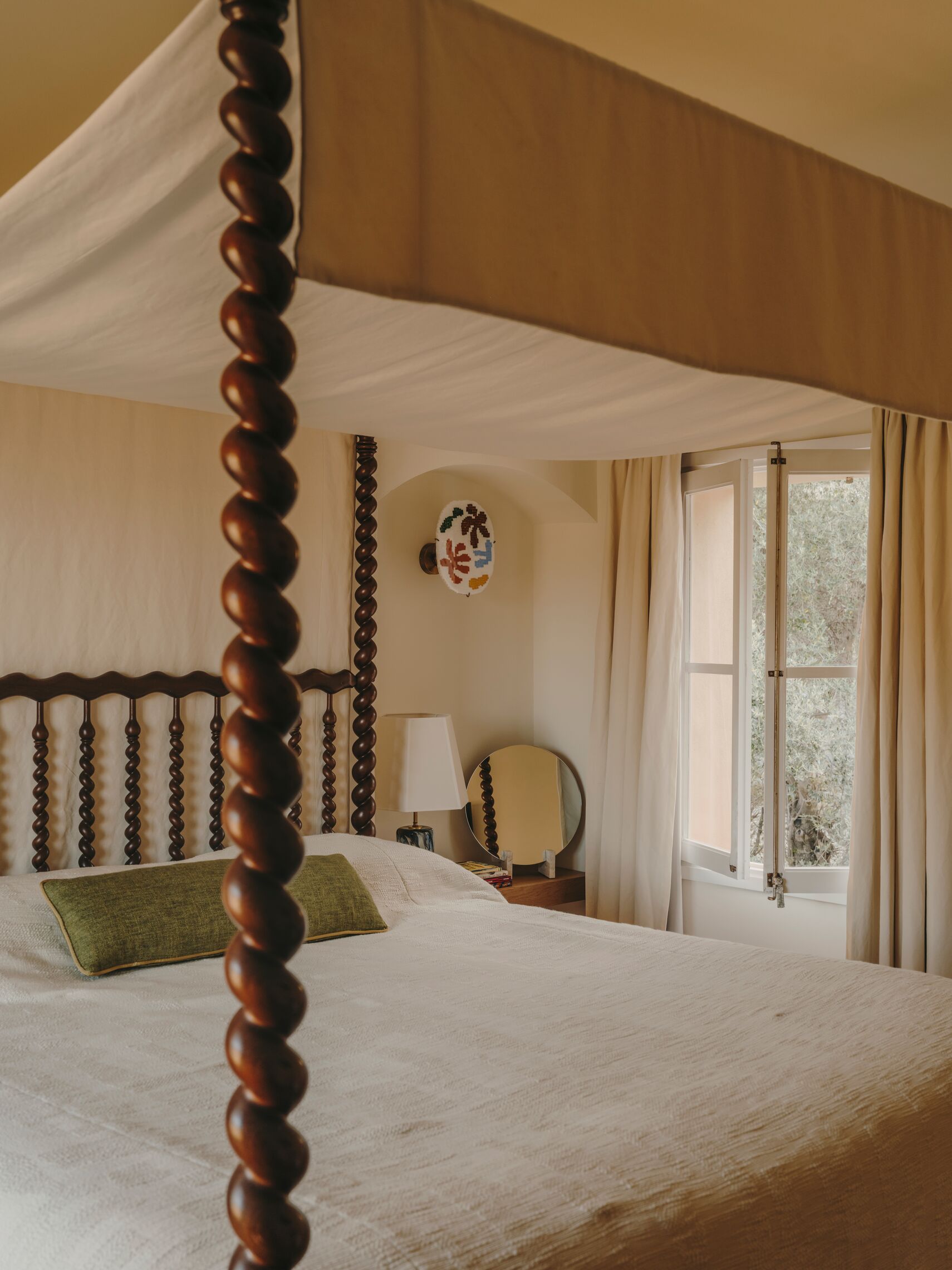 A transitional bedroom juxtaposes a canopy bed with swirling wooden structures with white linens and whimsical artwork.