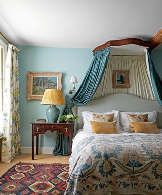 colorful bedroom with blue walls with half tester bed with blue canopy, mustard accents and patterned rug and curtains