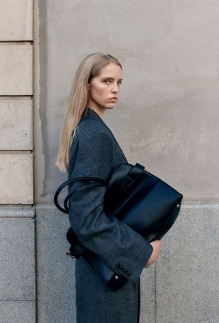 One of the best jacket coat brands, H&M, is shown in an image of a model wearing a gray coat with a large bag bag