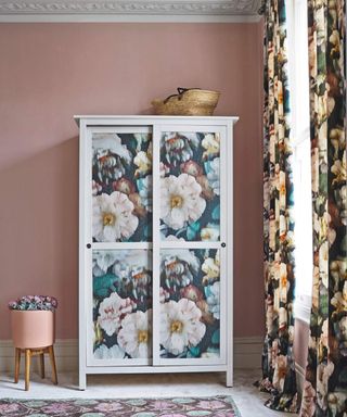 Wardrobe with panels decorated with large floral print against a pink wall with elaborate coving, floral curtains and rug.