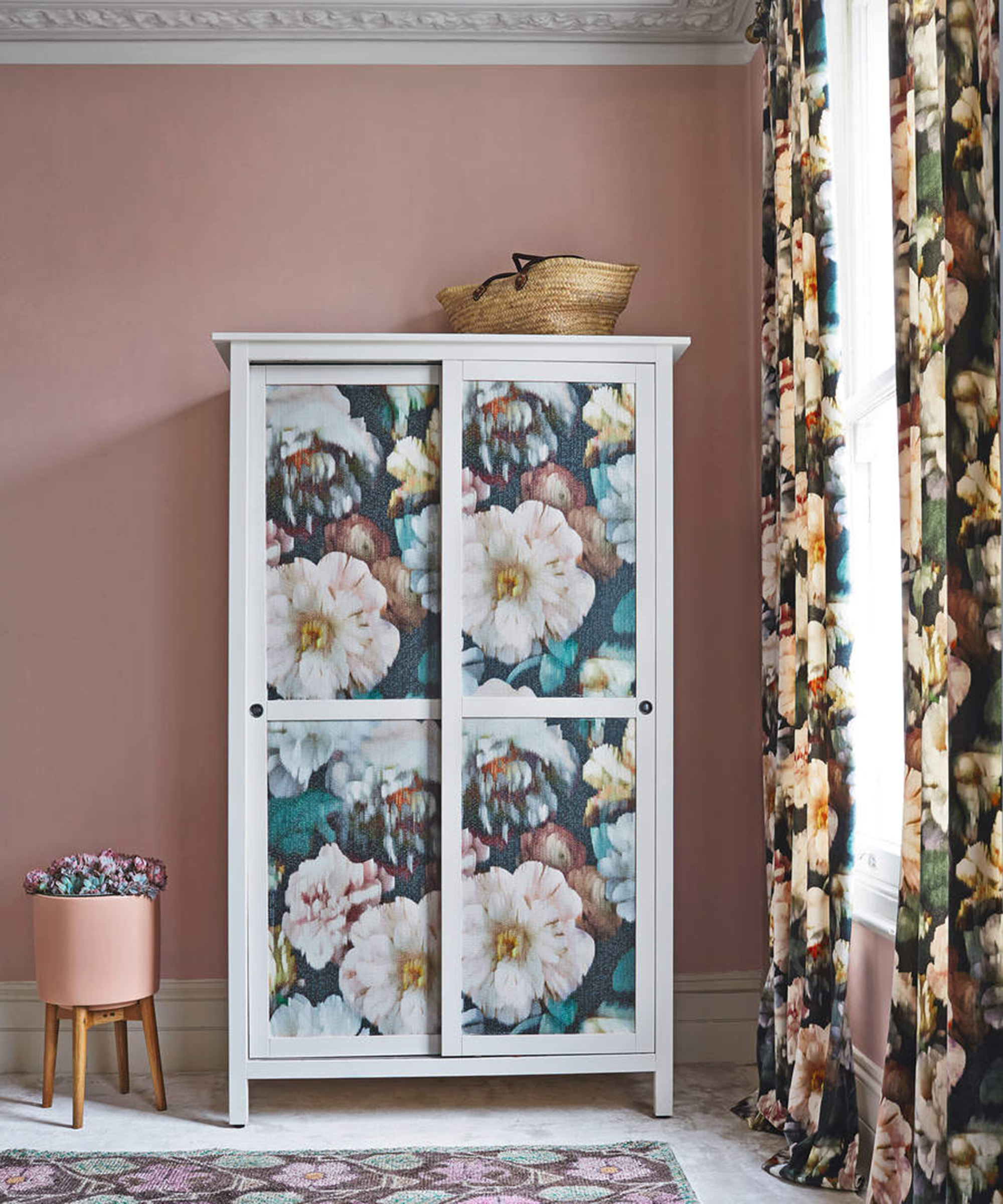 Wardrobe with panels decorated with large floral print against a pink wall with elaborate coving, floral curtains and rug.