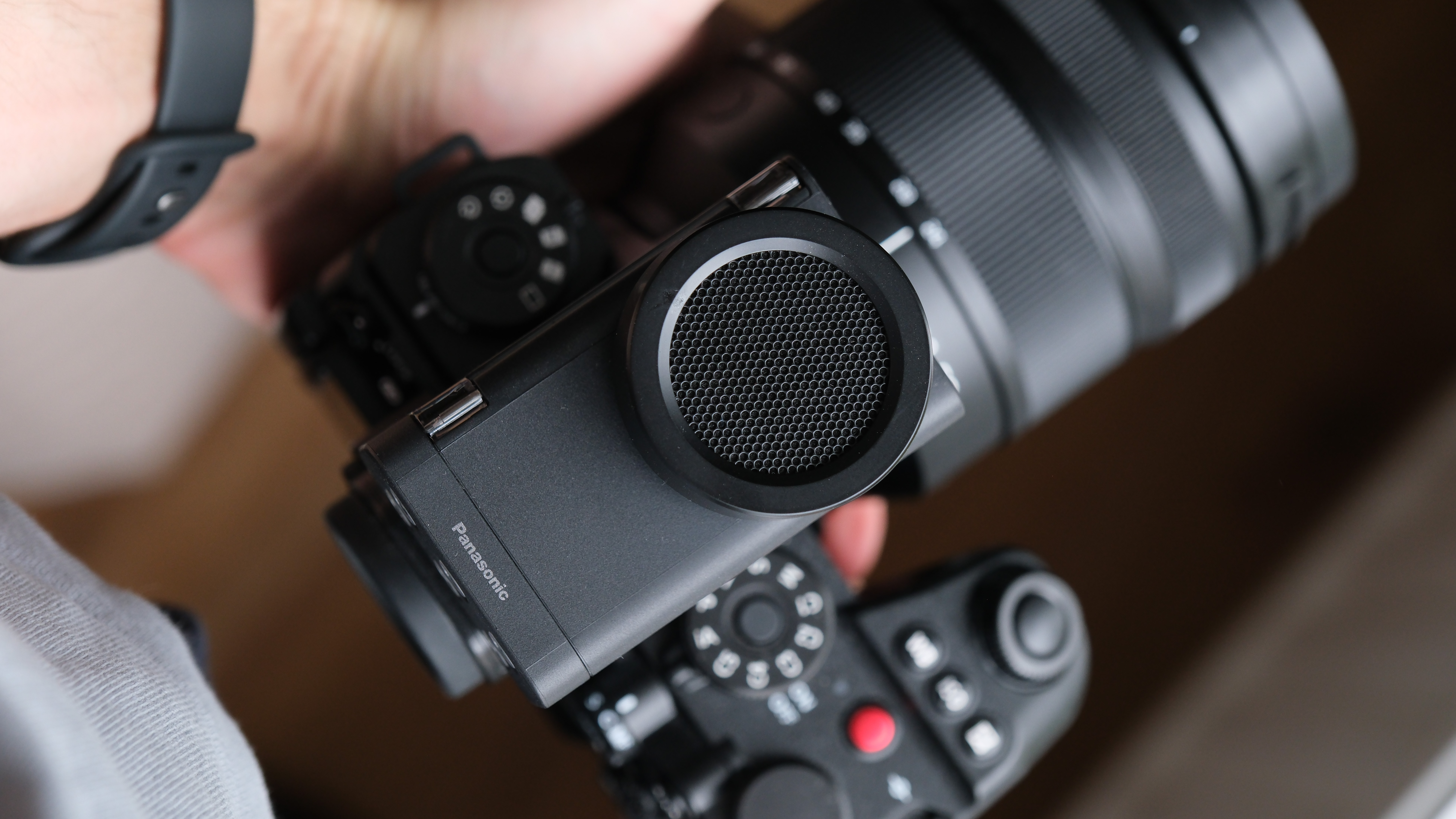 Angled view of the Panasonic Lumix DMW-DMS1 on a Lumix camera, showing the internal audio controls beneath the clear protective cover.