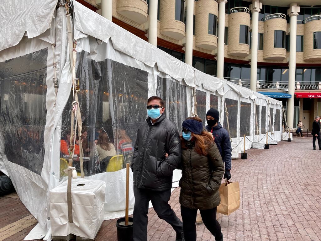 People walk past a plastic covered section outside an eating area at a restaurant in Washington, DC on February 14, 2021.