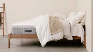 An image showing the Awara Mattress dressed with a white duvet and cream knitted throw