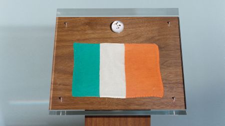 a wooden podium displaying four black pebbles inside a clear lucite ball and a green, white and orange flag