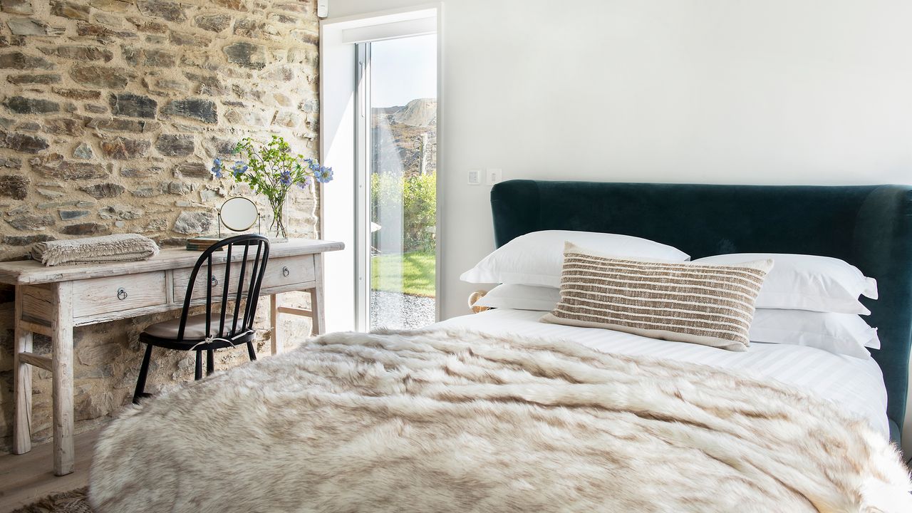 Bedroom with throw on bed, exposed brick wall and window into garden