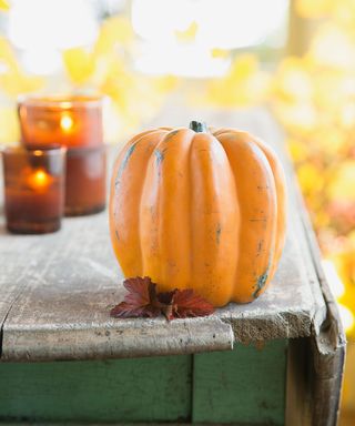 One pumpkin on a porch table outside with two candles burning in the background