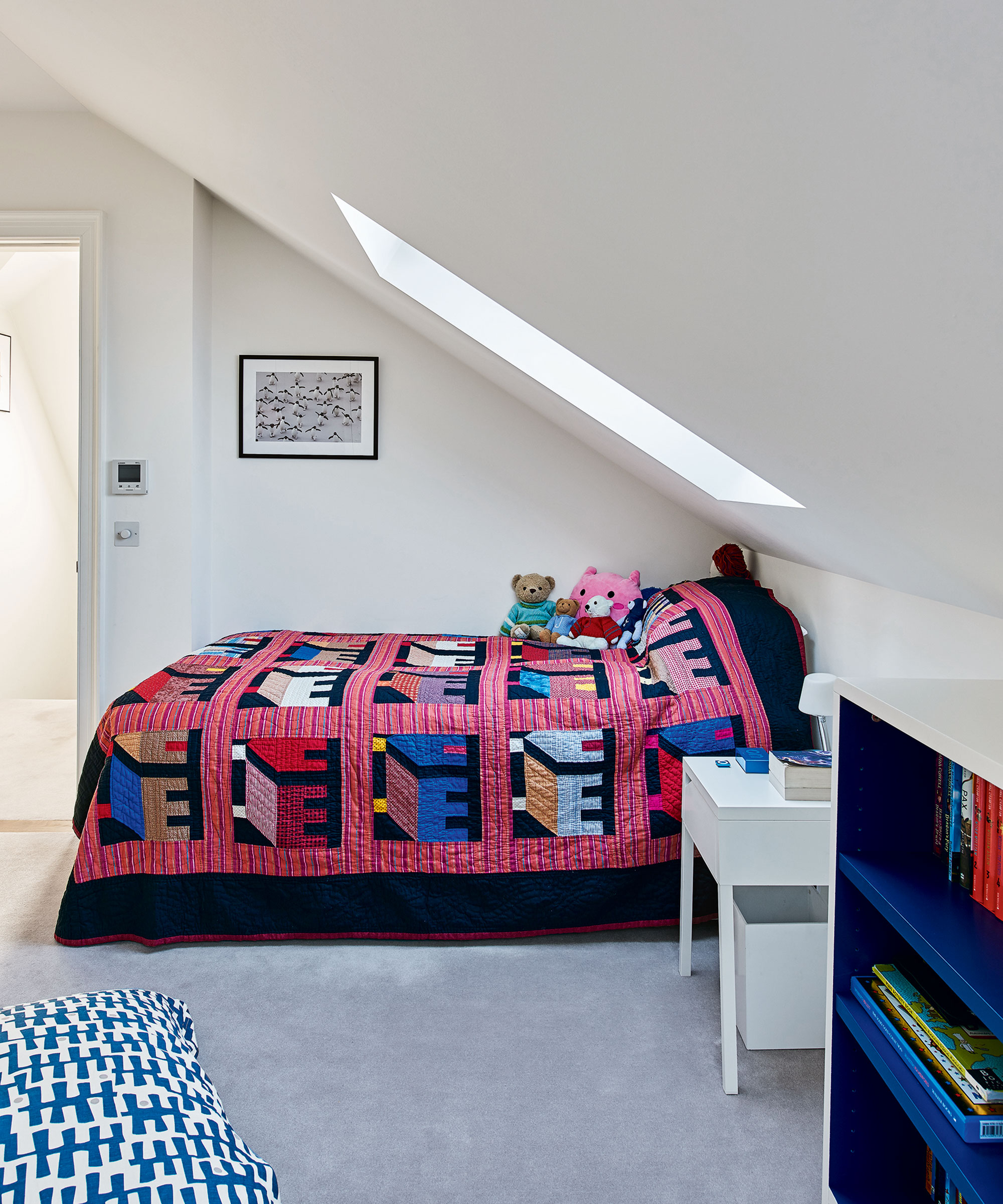 A white loft room with skylight over a single bed with red patterned quilt.