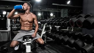 Musclular person having a shake while sitting on a weight bench in a gym