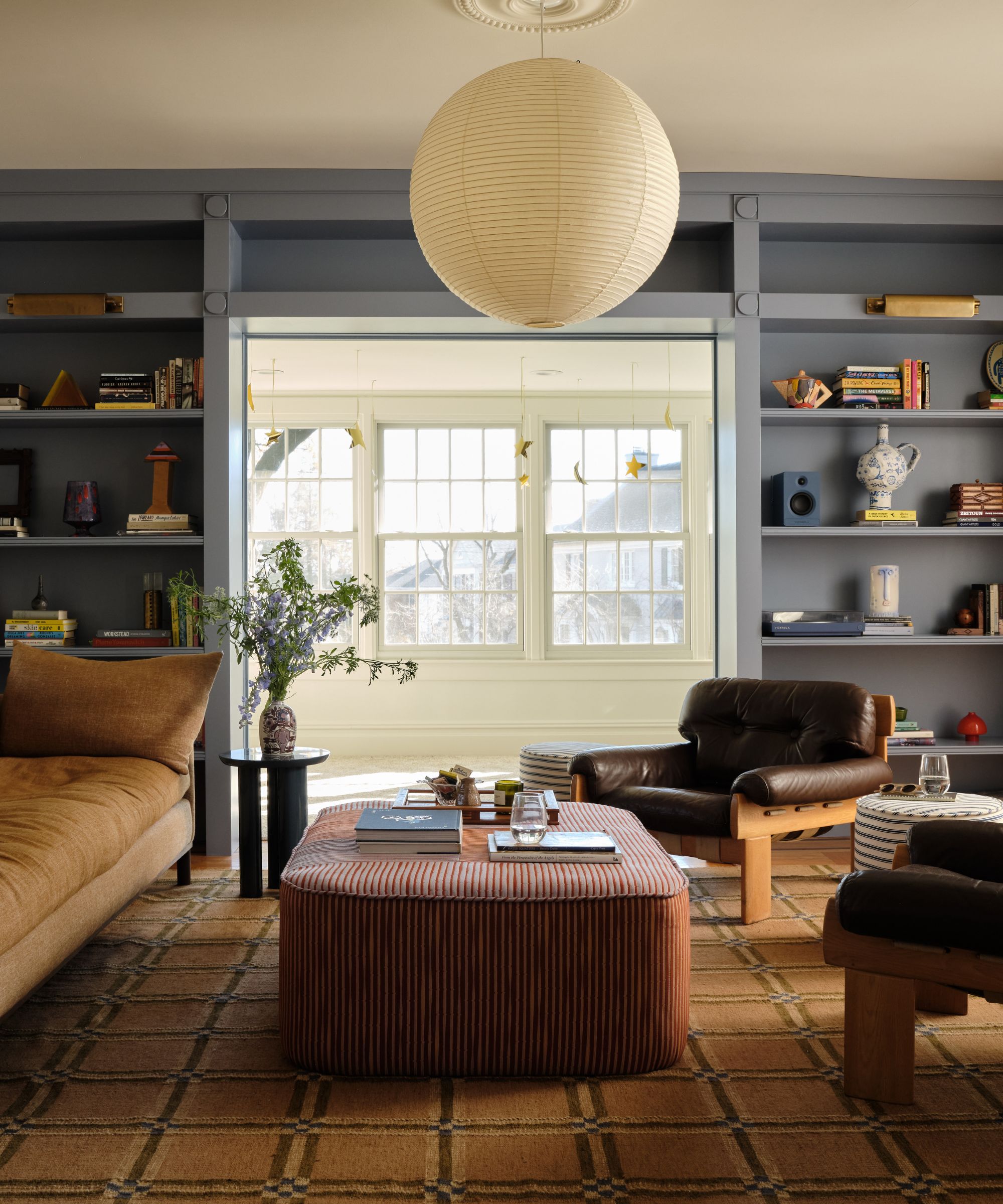 a small living room in new jersey with large windows, custom blue bookcases, a west elm rug, and vintage style 1970s sofa and leather armchairs