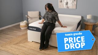A woman sitting on the end of the Nectar Classic mattress in a bedroom, with a Tom's Guide 'PRICE DROP' badge overlaid