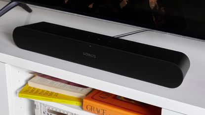 Sonos Ray soundbar on white TV stand, with colorful books pictured on shelf underneath.