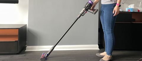 A woman holding the Dyson Micro 1.5kg in a room with grey walls and grey wood floors