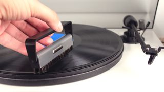 A turntable with a hand holding a cleaning brush, cleaning the vinyl 
