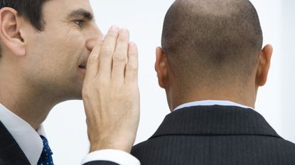 A business man whispers a secret into another businessman&#039;s ear.