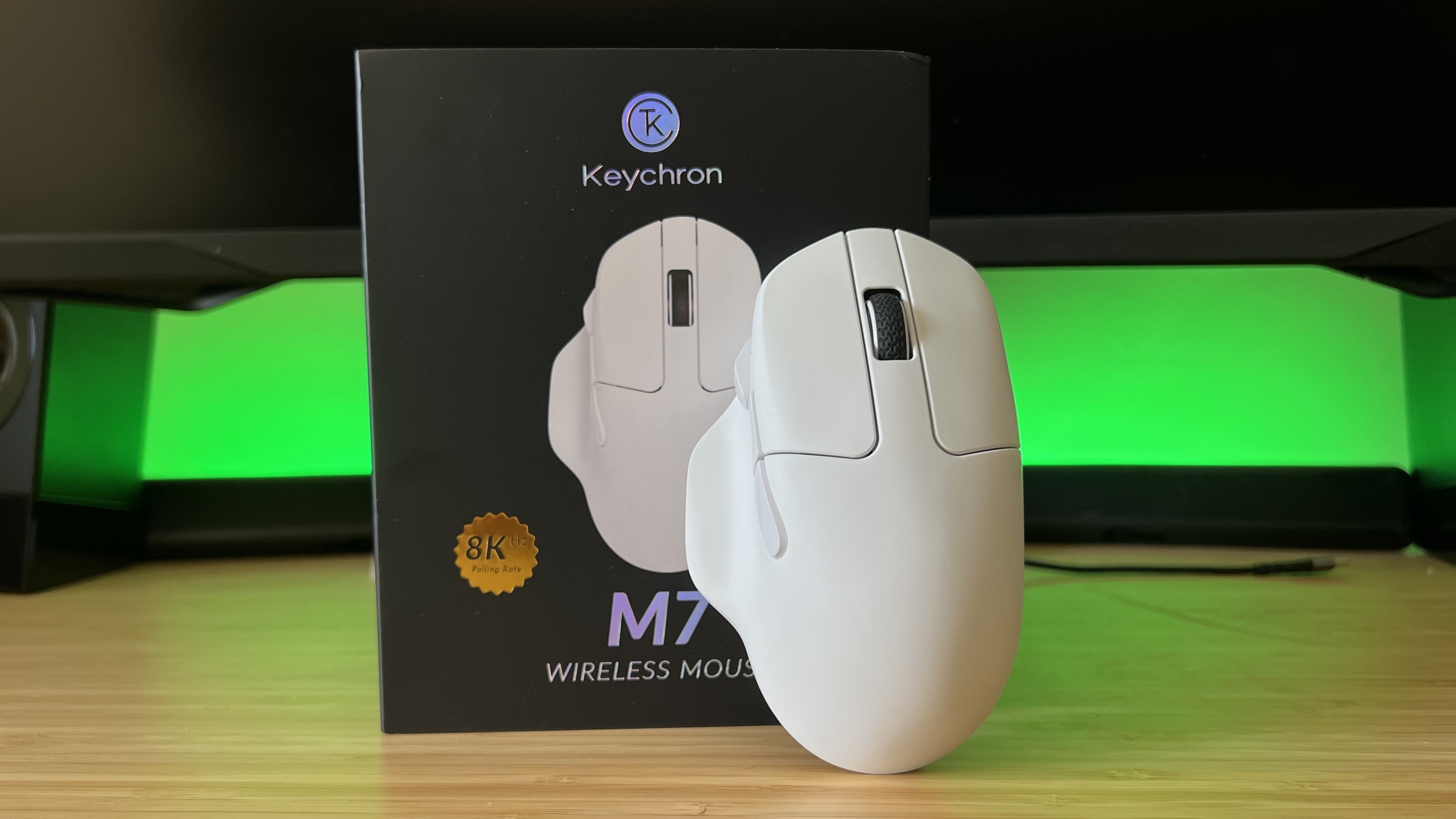 Keychron M7 8K gaming mouse leaning against packaging on a wooden desk with green lighting