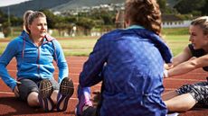 Three women sitting on running track stretching