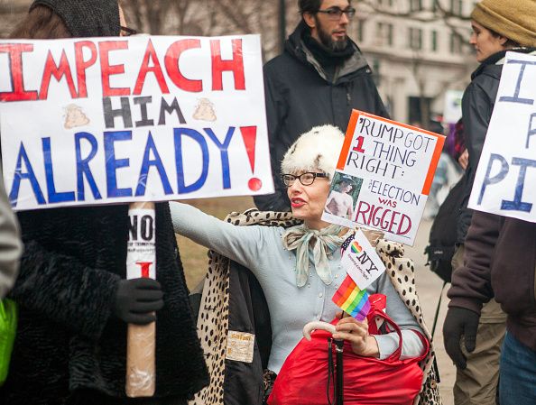 Demonstrators protest President Trump with signs challenging his legitimacy. 