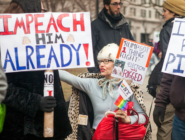 Demonstrators protest President Trump with signs challenging his legitimacy.