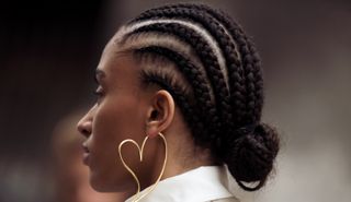A guest wears cornrow braids, white shirt and beige trench coat and a heart shape statement earring outside Victoria/Tomas during the Womenswear Fall/Winter 2024/2025 as part of Paris Fashion Week on February 27, 2024 in Paris, France.