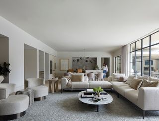 neutral open plan living space with neutral sectional sofa, floor length curtains, oval coffee table and gray patterned rug