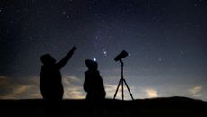 two people stood next to tripod mounted binoculars against the night sky