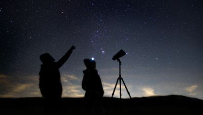 two people stood next to tripod mounted binoculars against the night sky