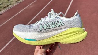 Hoka Mach X2 running shoes in a person's hand on a running track