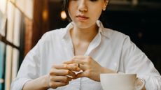 A serious-looking woman in a coffee shop contemplates taking off her wedding ring.