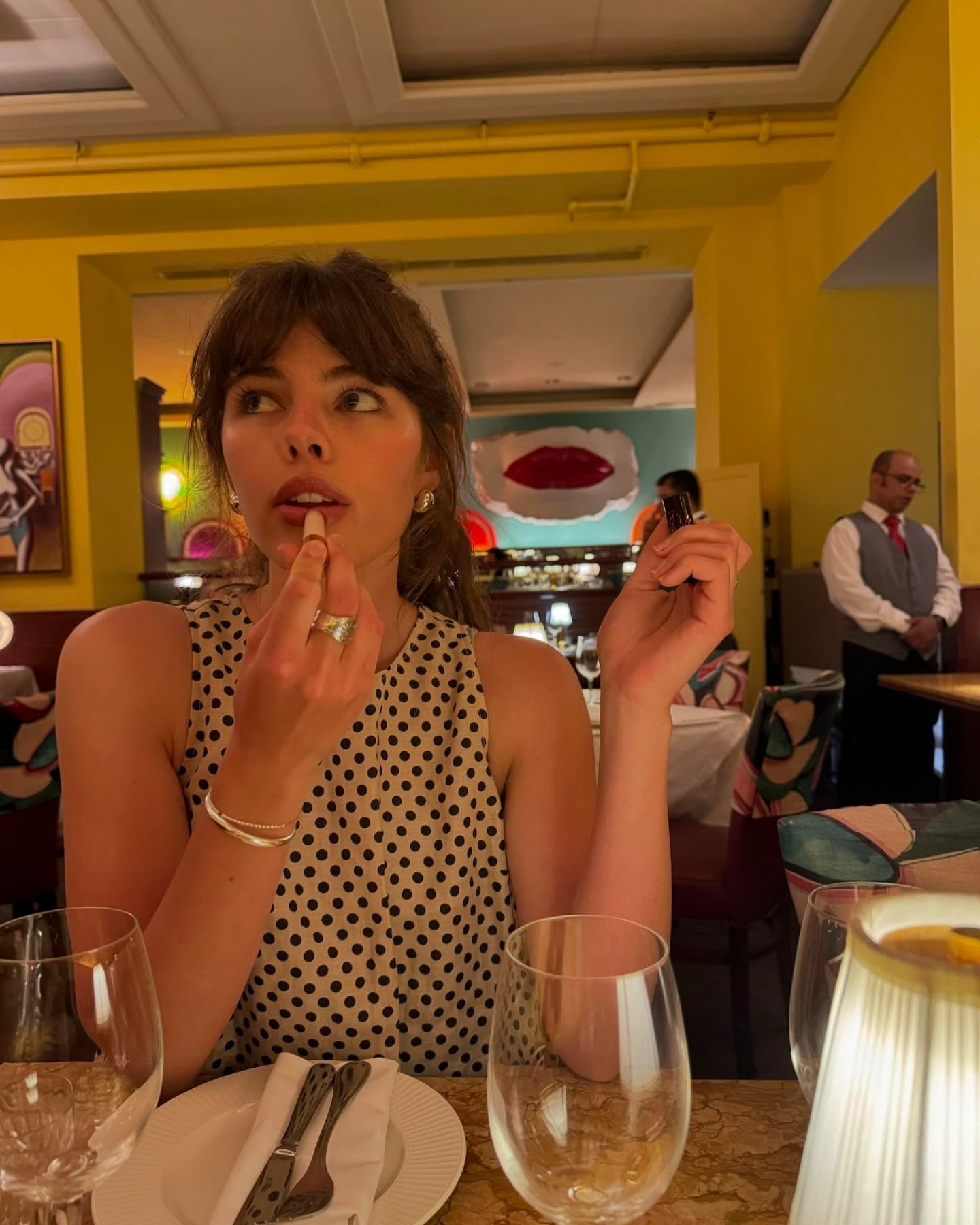 A woman applying lipstick in a restaurant.