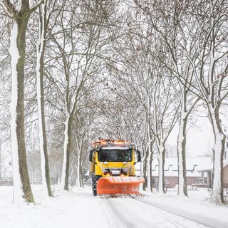 A snowplow clearing and gritting a snowy road surrounded by trees