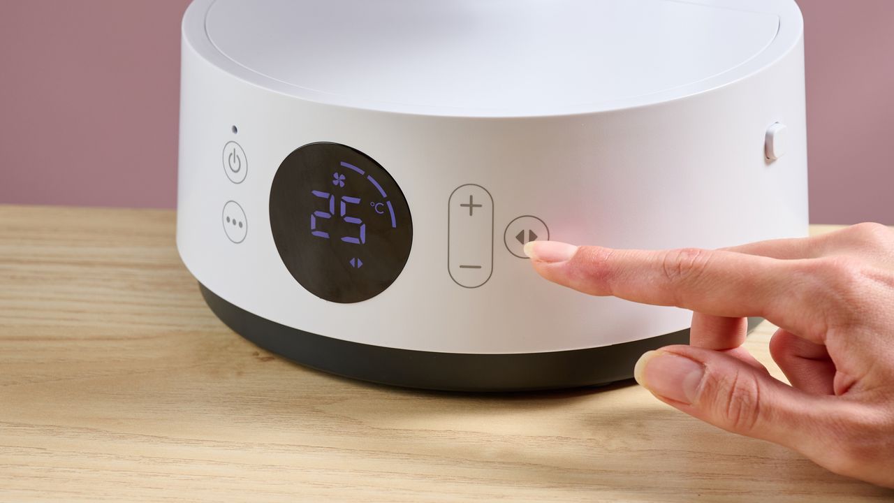 A woman is pressing the button to get the fan to oscillate.