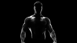 The silhouette of a muscular person in a dark photo studio