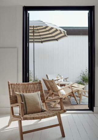 door open to patio with wooden armchairs and striped parasol