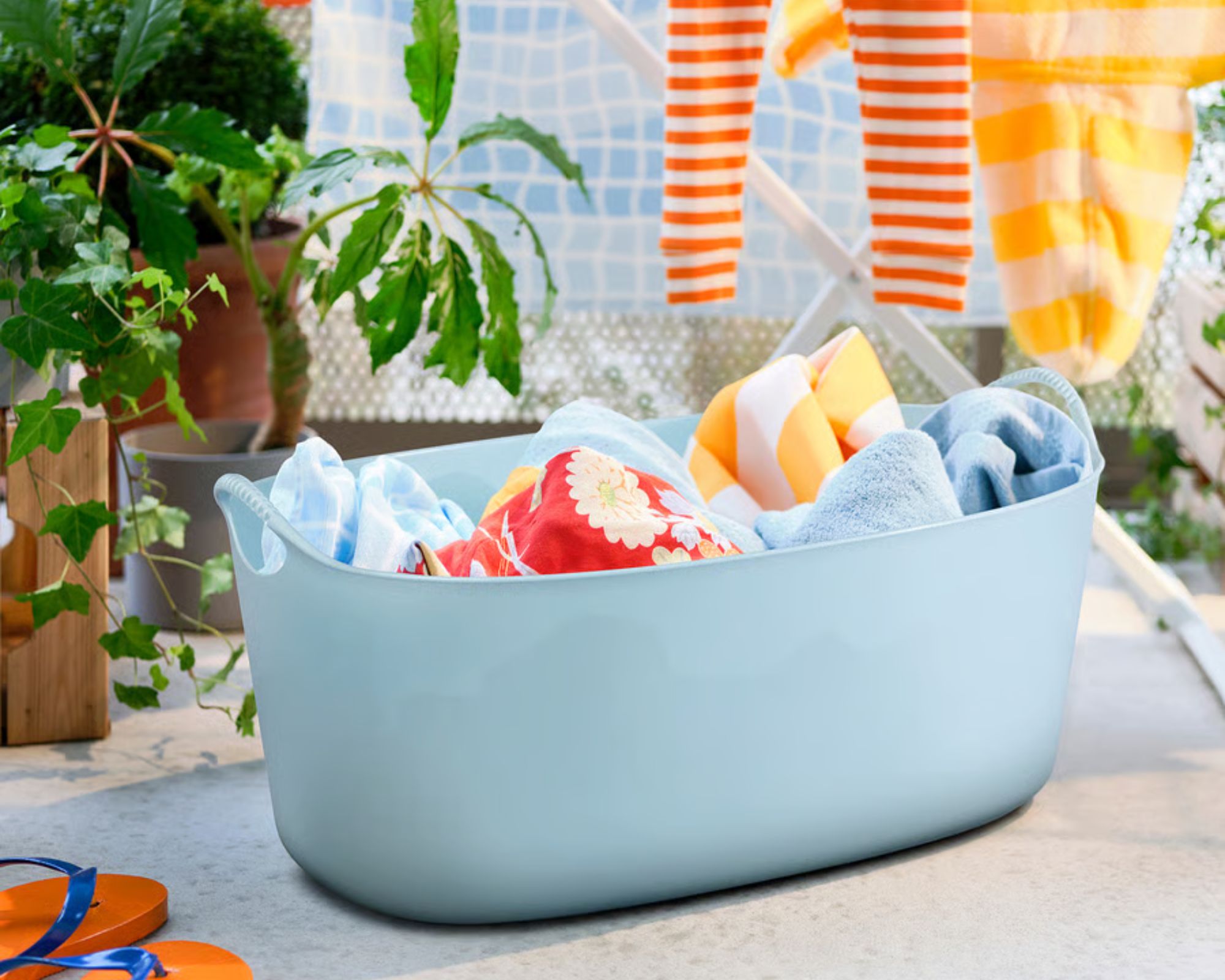 IKEA TORKIS Flexible Laundry Basket pictured in a sunny garden with orange striped laundry and green plants.