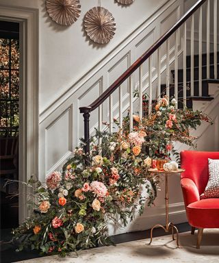 Christmas stair decor ideas with a floral arrangement at the base of the bannisters with winter flowers in pinks, reds and oranges