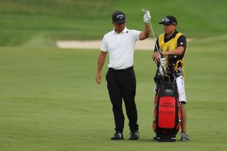 Xander Schauffele takes a club out the bag whilst chatting to his caddie