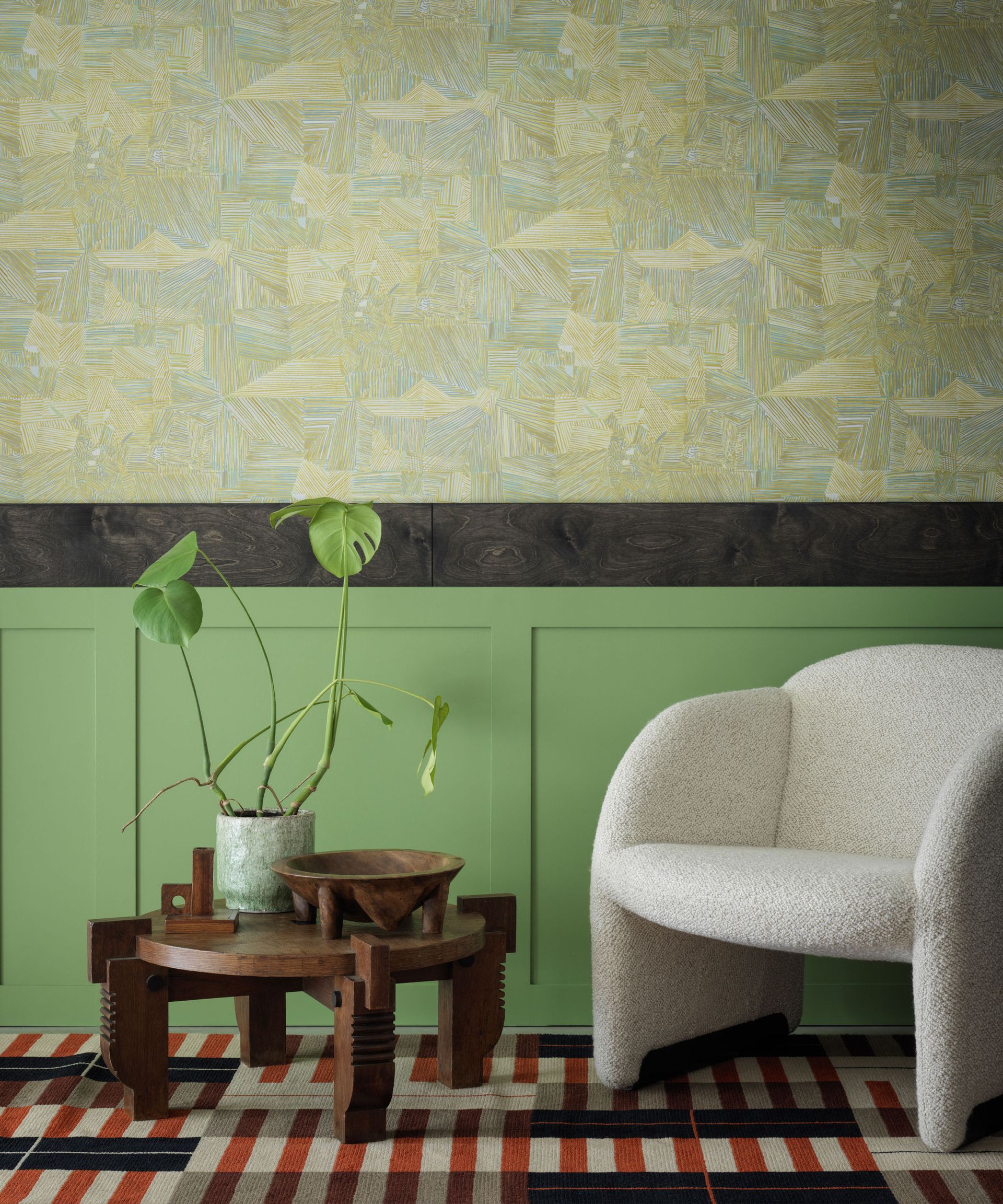 Living room with dado atelier wallpaper in matthew burrows sterno wallpaper, painted green paneling, boucle lounge chair, dark wood coffee table, red, cream and black striped rug