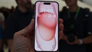 En hand håller upp en rosa iPhone 15 med skärmen vänd mot kameran.