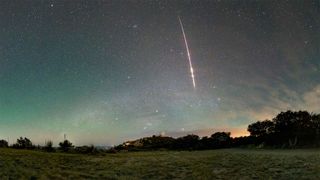 a red-tinted streak from a meteor plunges through a greenish-blue sky above the dome of an astronomical observatory