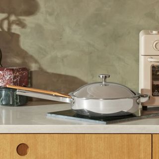 A stainless steel frying pan with a matching lid on a stone kitchen counter