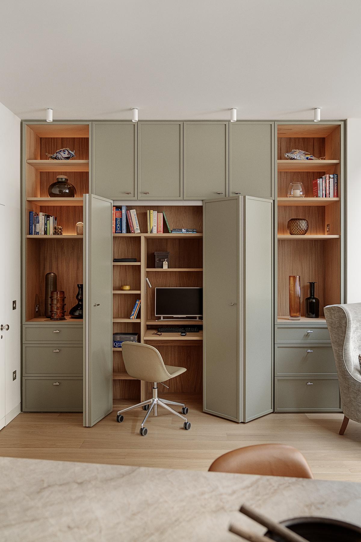 A living room office with sage green painted cabinets, timber inserts, light timber floors, shelves styled with books and vases
