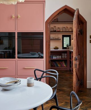 kitchen with pink units and arched wooden door leading to walk in pantry