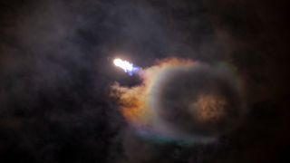 a spacex falcon 9's engines burn bluish-white against a swirling cloud pattern in the night sky.