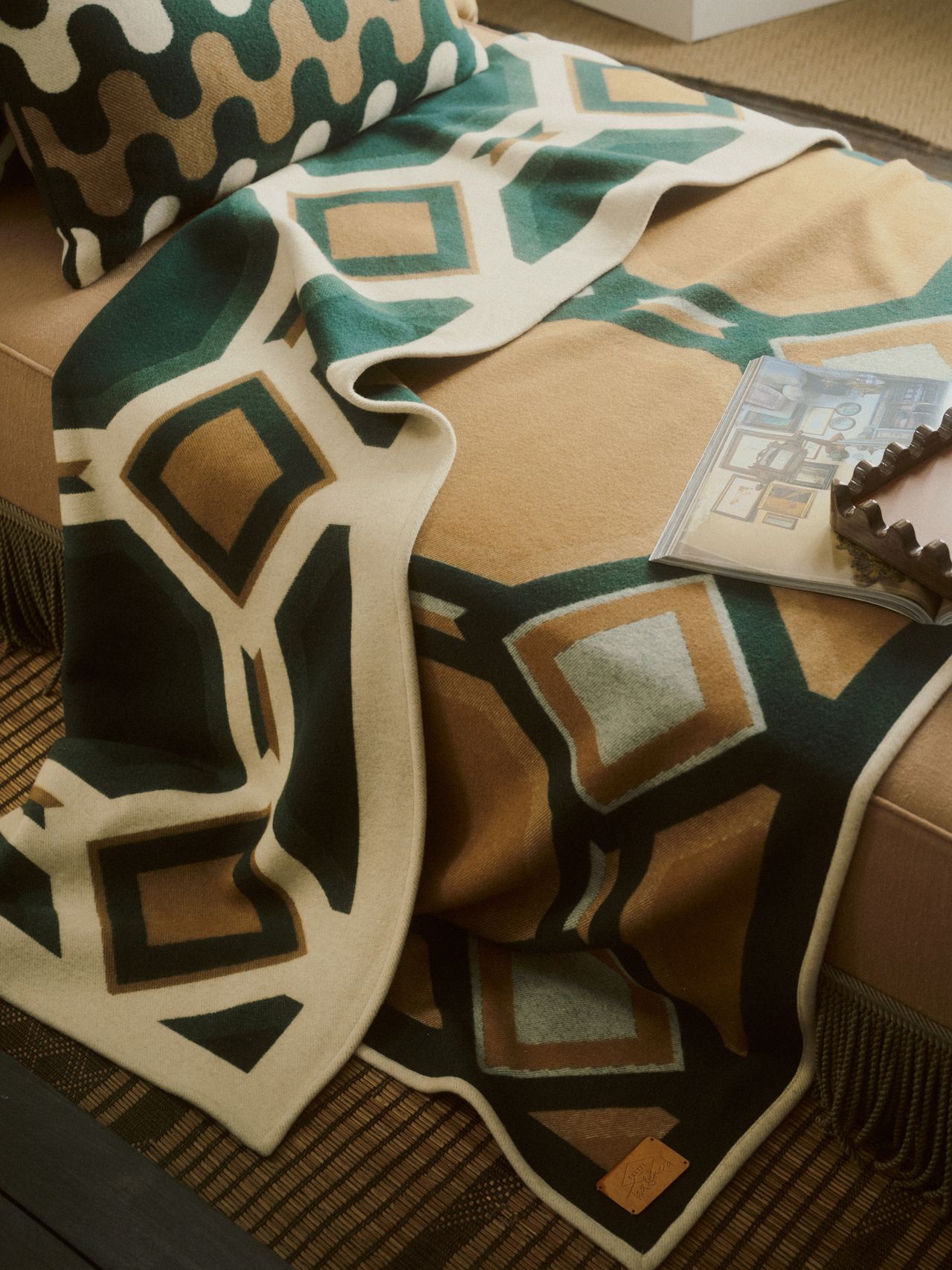 Close-up of an emerald, tan, and off-white geometric print throw blanket lying across a bench seat.