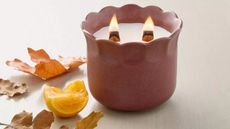 Burgundy scalloped candle on a wooden table next to fall foliage