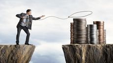 A businessman standing on a cliff tries to lasso stacks of coins across an abyss.