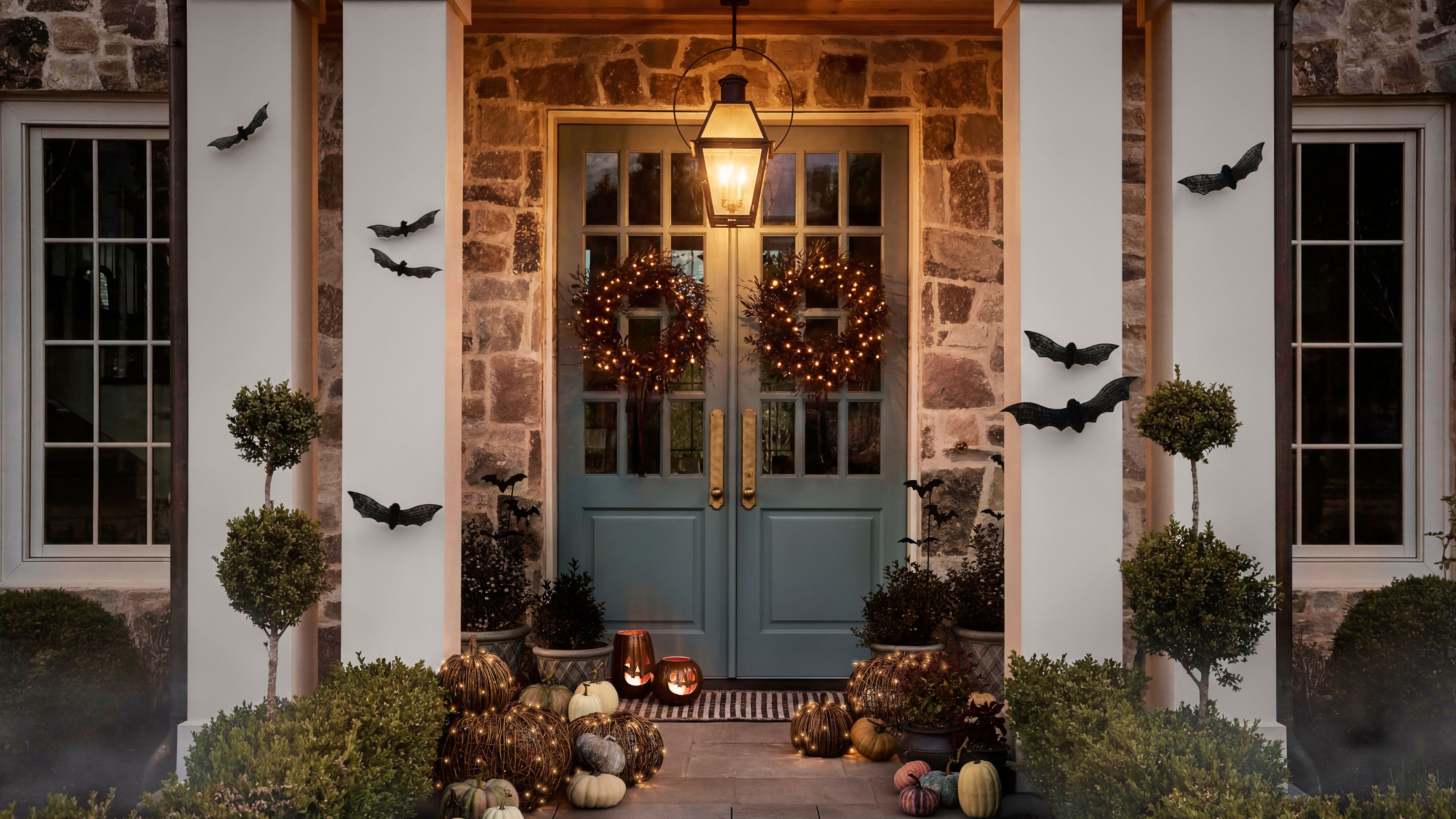 Charming entryway decorated for Halloween with wicker bat wall hangings, scattered pumpkins, and gothic wreaths