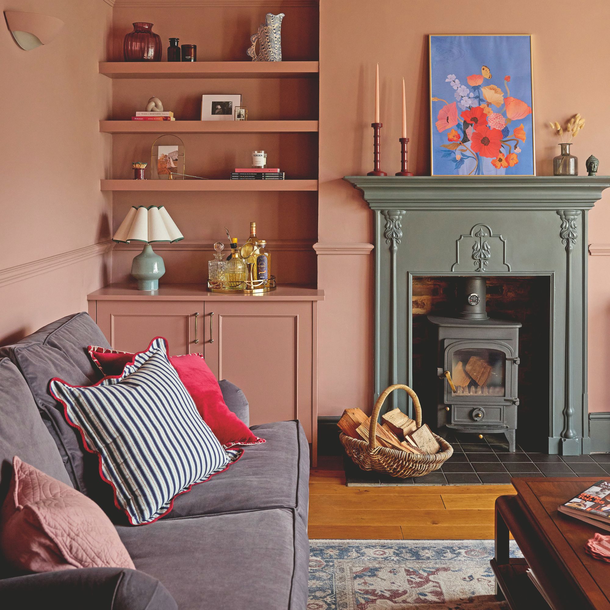 Pink living room with a log burner and a grey sofa , and pink units built into the alcoves